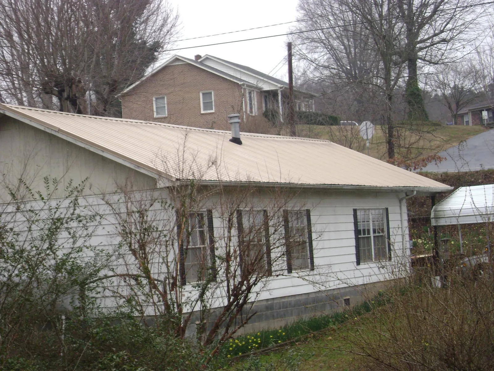 Tan metal roof on a white sided house set into a hillside — Commercial Roofing by Roofing Brothers in Lakewood