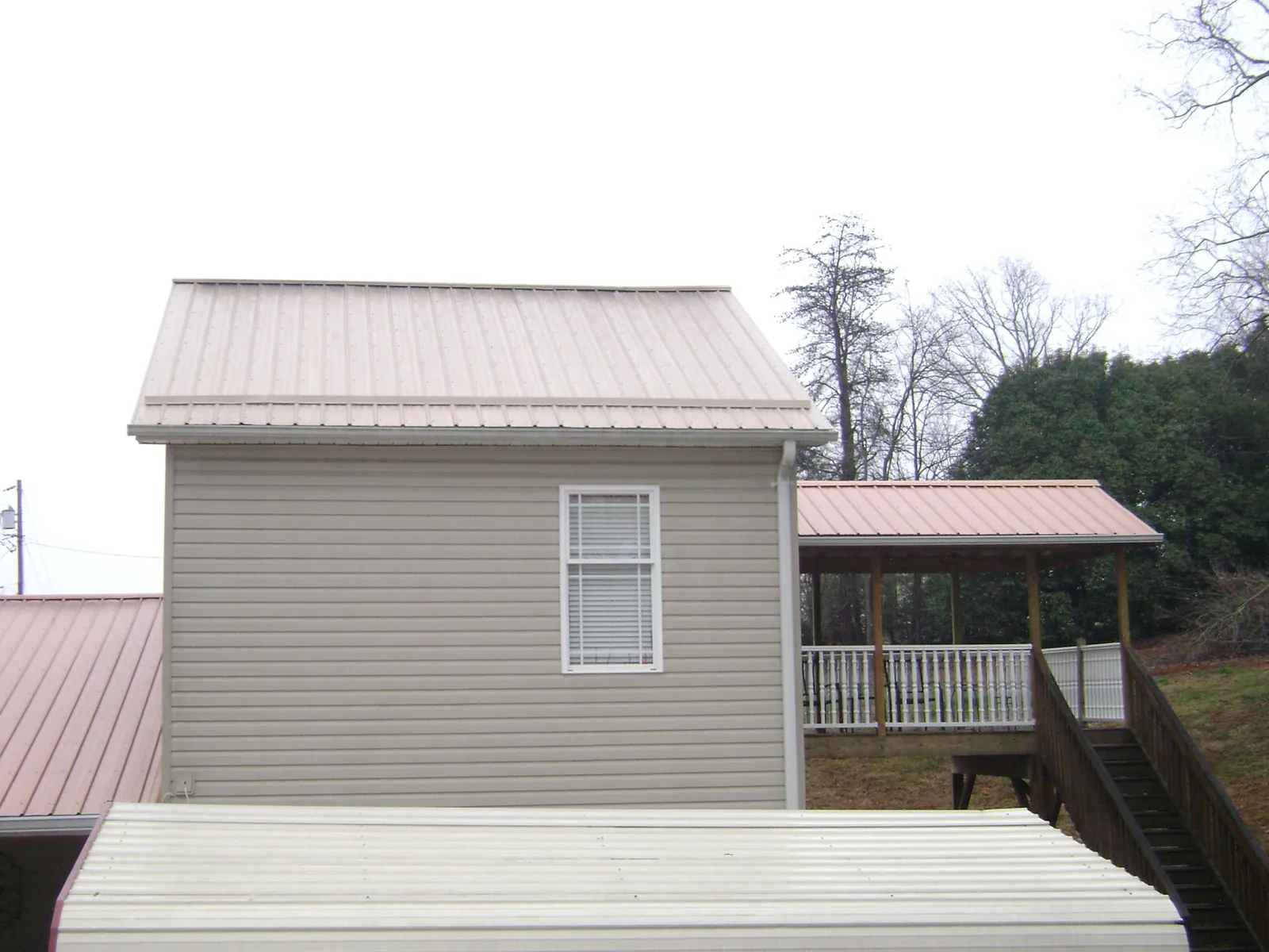 Tan metal roofs on a two story addition and attached porch, from a Roof Replacement job in Lakewood